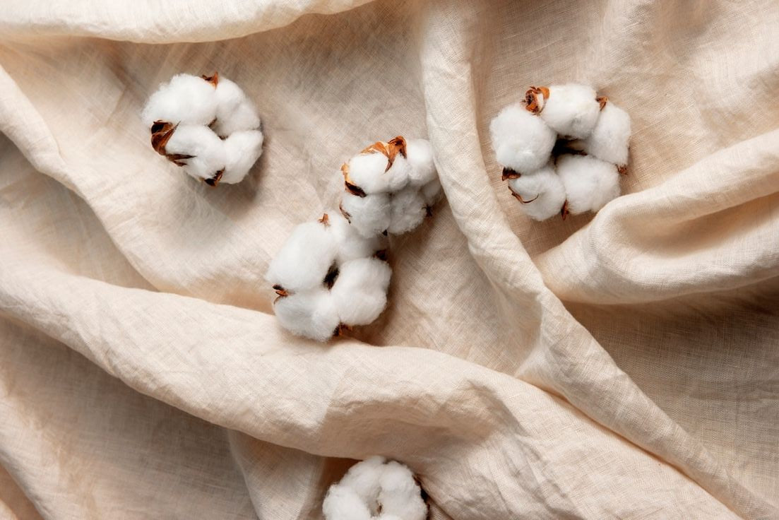 Boules de coton naturelles disposées sur une toile beige, représentant l’origine des tote bags en coton biologique.