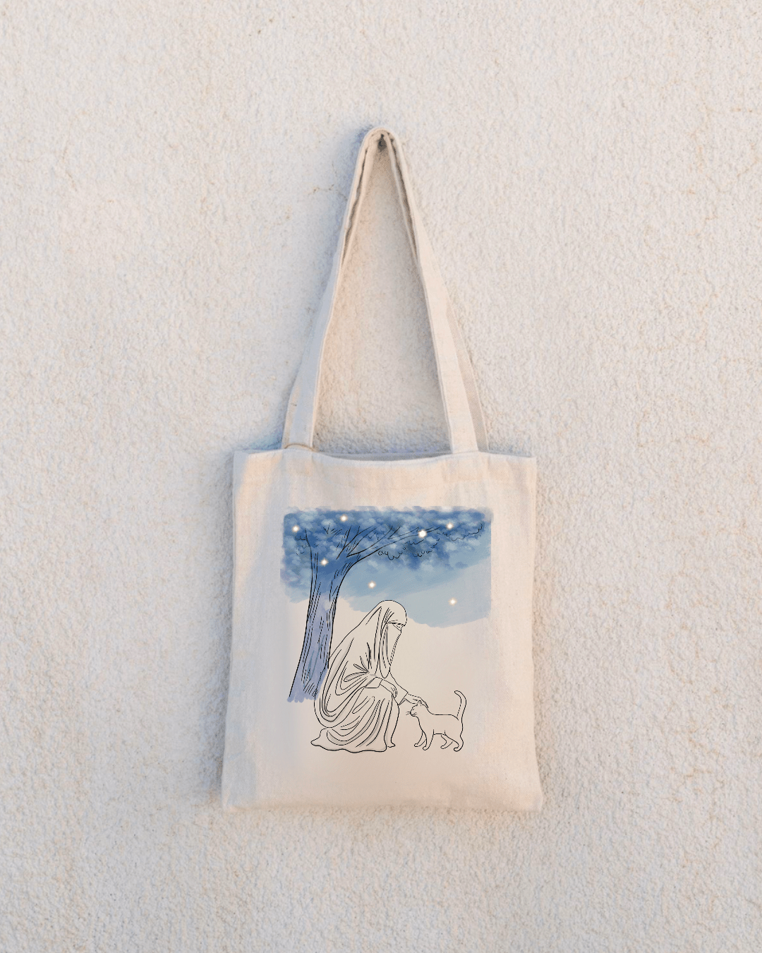 Close up d'un tote bag collection neutral de la marque senistuff, une femme portant un niqab caresse un chat près d'un arbre