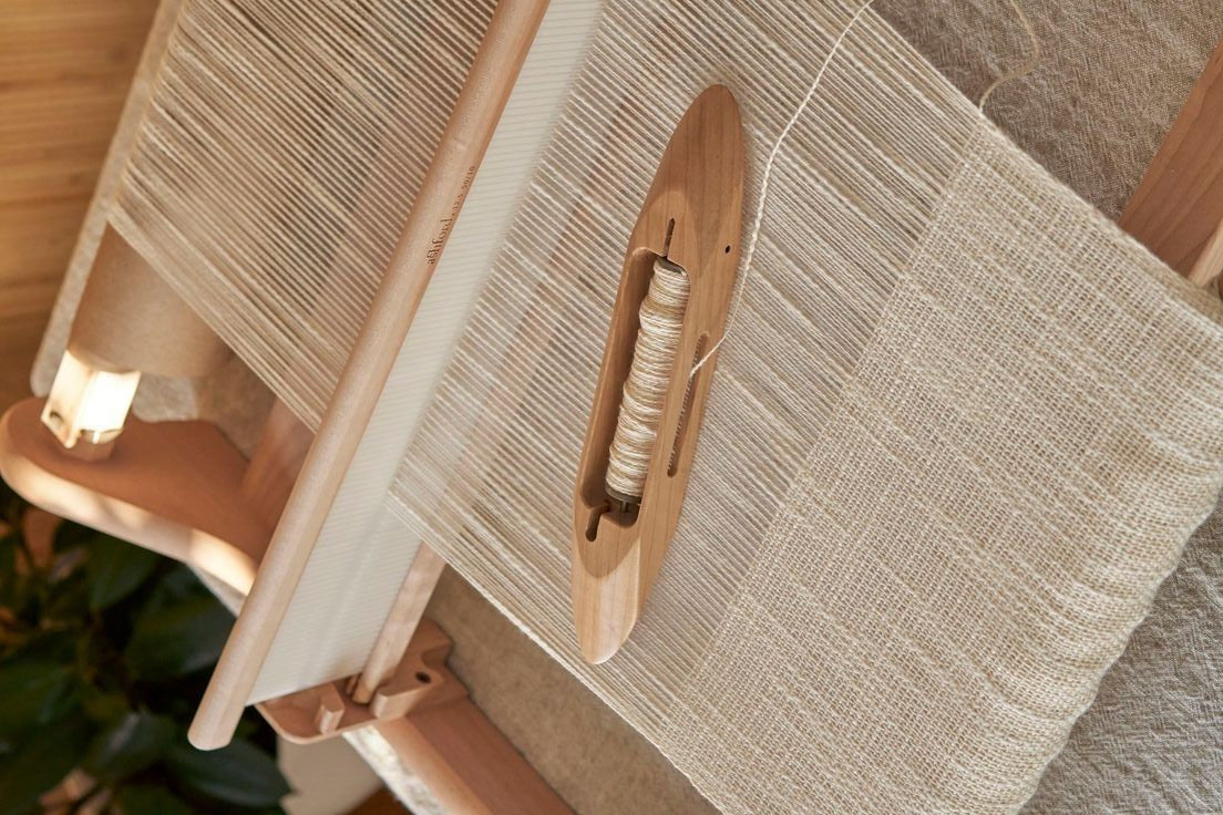 Métier à tisser traditionnel en bois avec trame de coton naturel, illustrant le processus artisanal de fabrication textile.