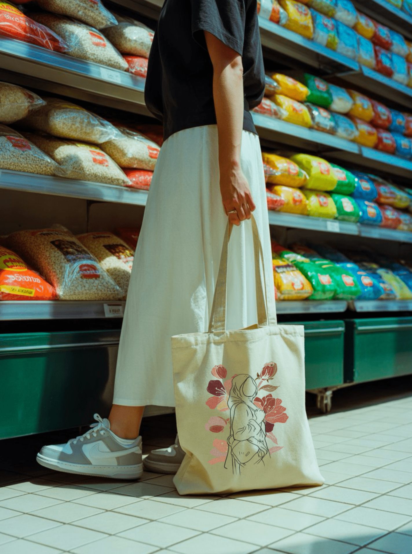 Sac en toile porté dans une allée de supermarché, décoré d’une illustration féminine avec un motif floral rouge vif.
