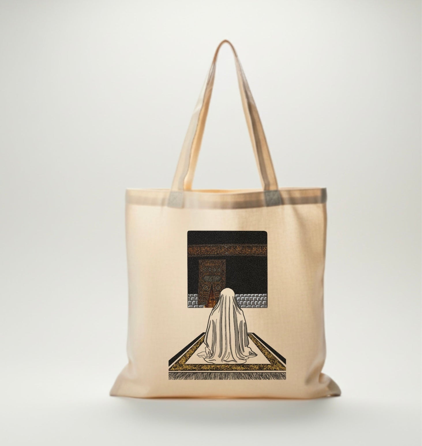 Sac en coton beige avec illustration d’une femme voilée en prière devant la Kaaba, design spirituel en noir et or.