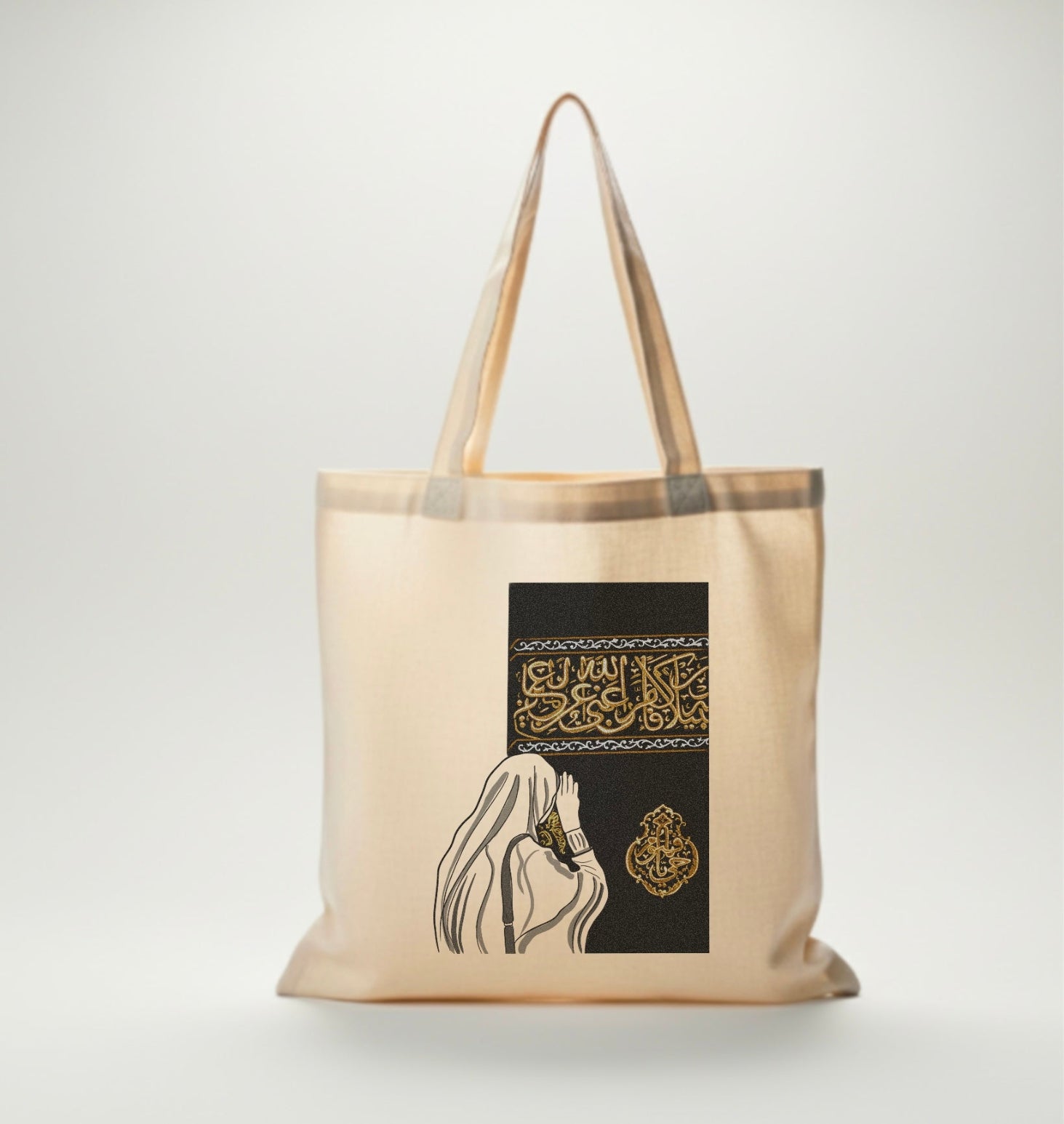 Sac en toile beige Seni’Stuff avec illustration d’une femme voilée face à la Kaaba, motifs noirs et dorés raffinés.