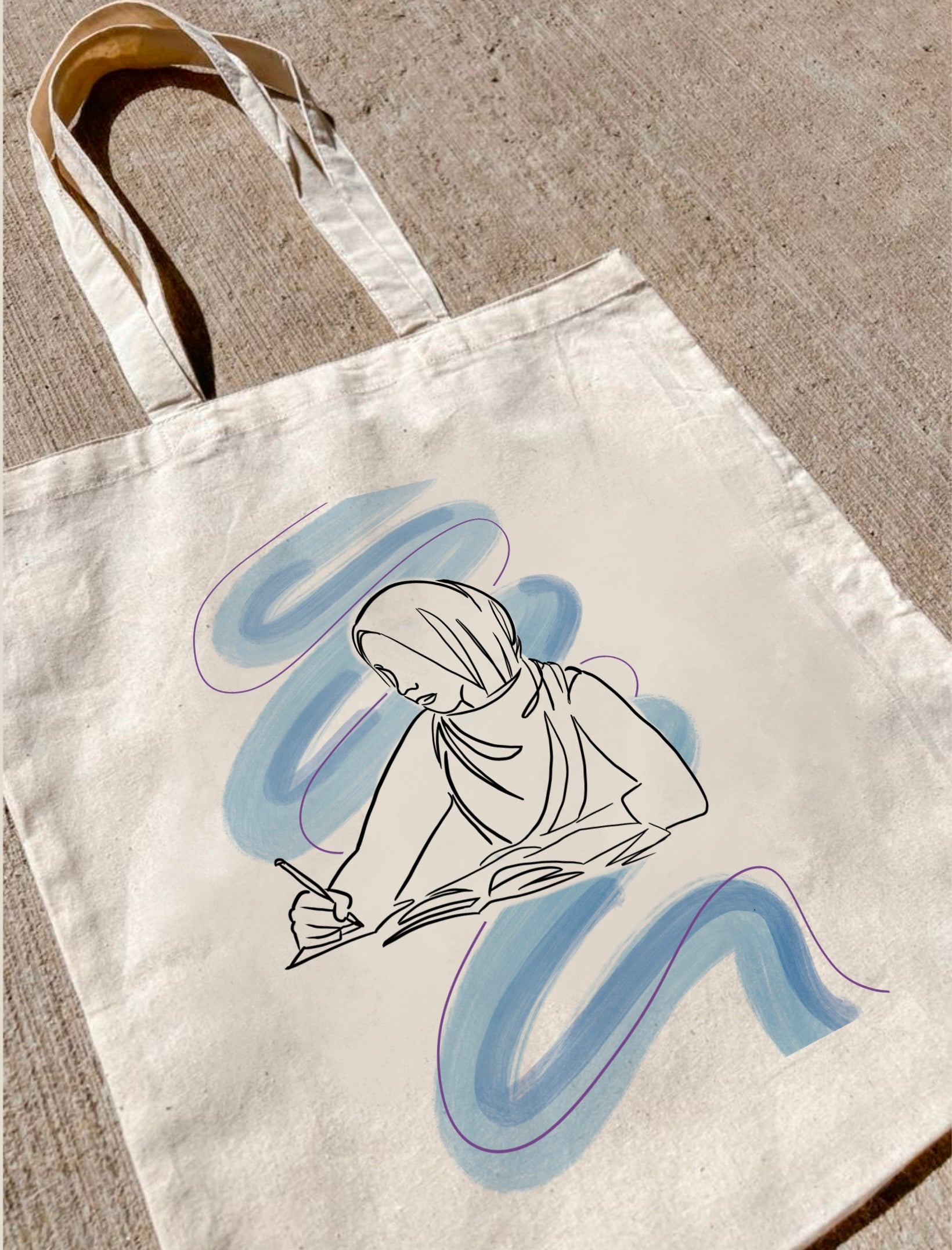 sac en toile Seni'Stuff avec dessin d’une femme musulmane en train d’écrire, posé sur le sol
