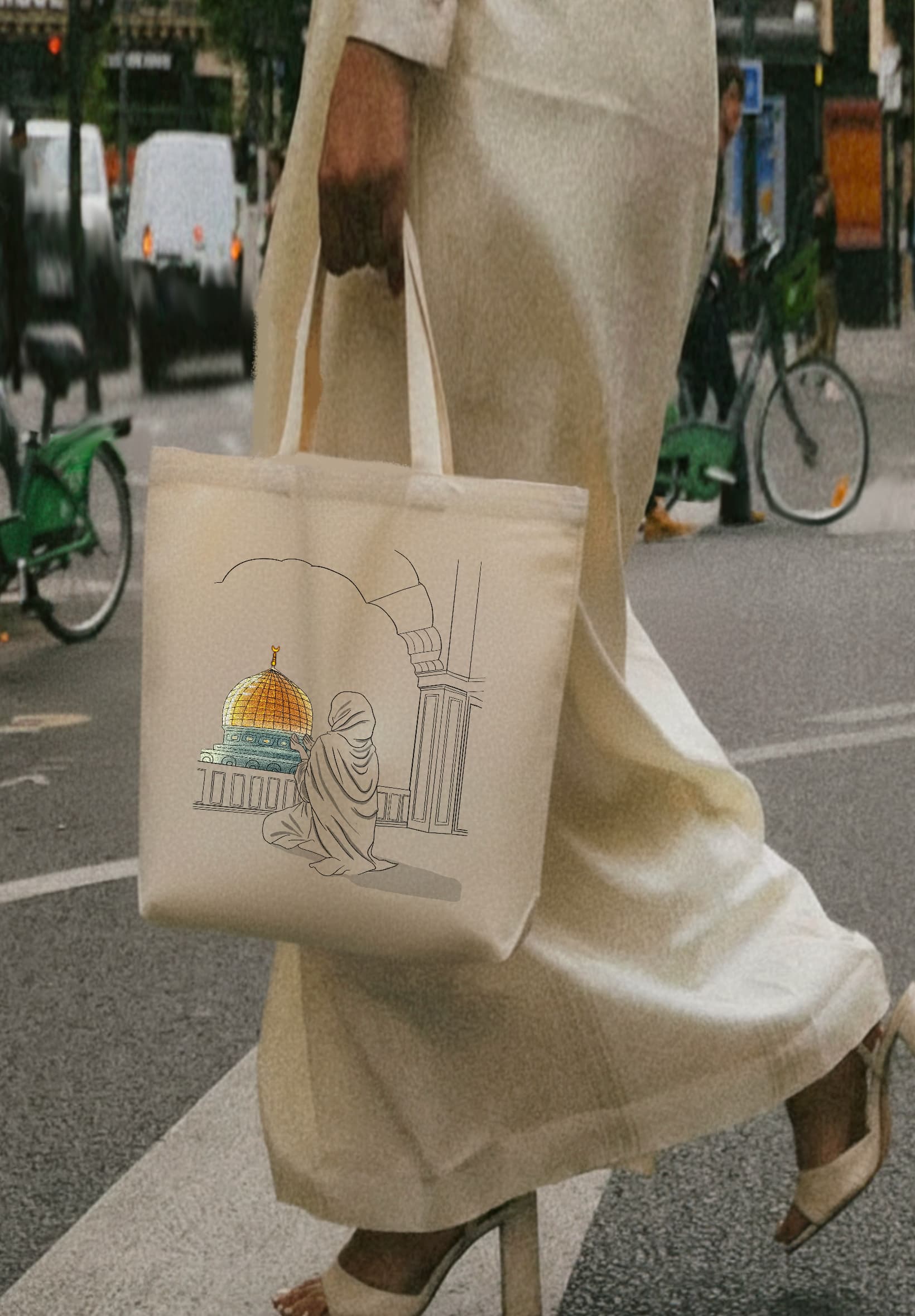 vFemme marchant en abaya beige dans la rue, portant un tote bag Seni'Stuff illustré du Dôme du Rocher à Jérusalem.